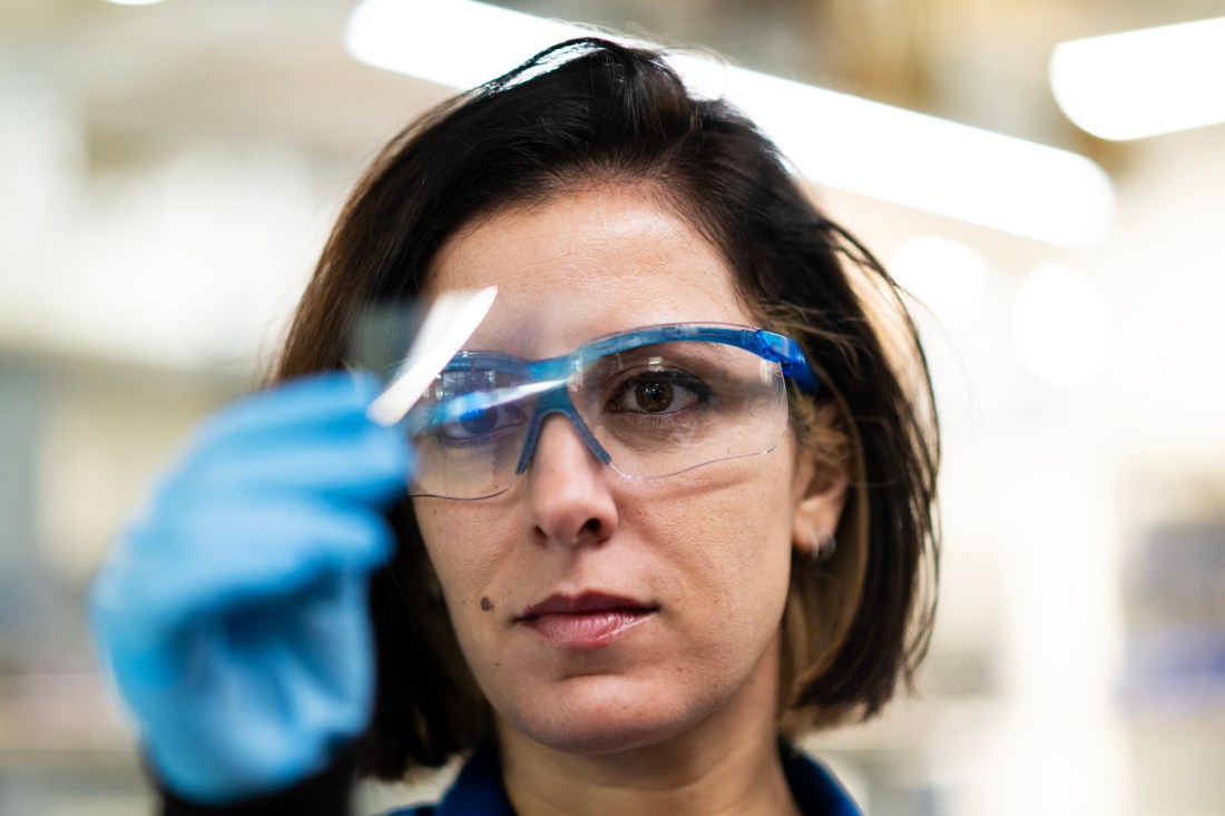 Leila Deravi wearing lab glasses in the lab holding a piece of material up in front of her. 