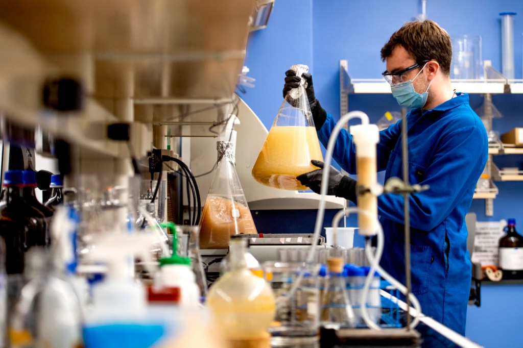 Robbie Green holding up a large beaker of orange colored substance in a lab.