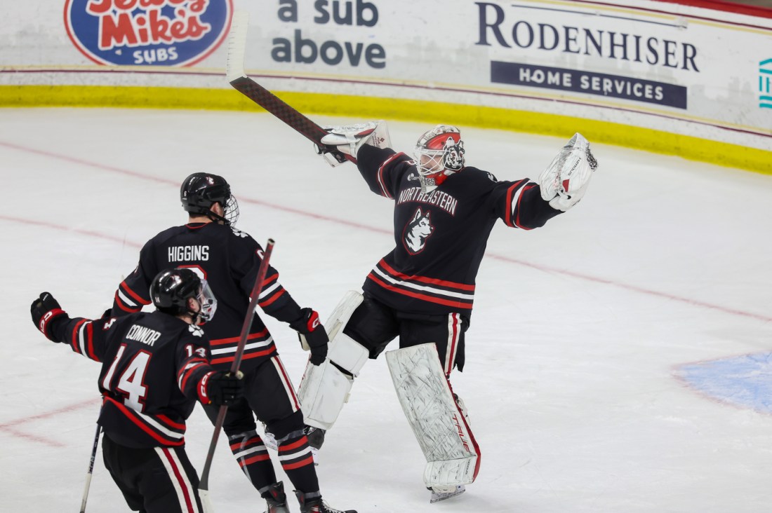 Northeastern goalie cheering with his arms raised while skating over to two teammates.