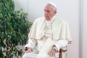 Pope Francis wearing white robes sitting in a chair next to a plant.