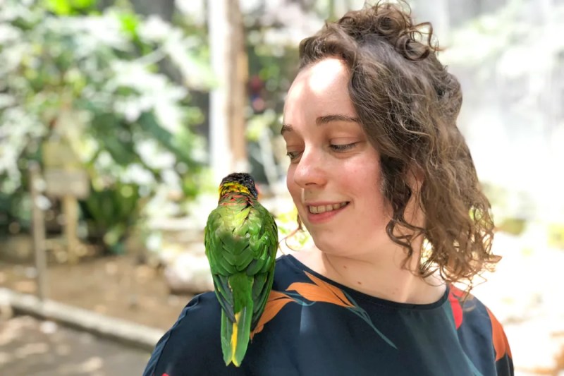 Portrait of Rebecca Kleinberger with a parakeet on her shoulder.