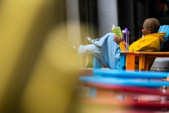 A person sits on a blue lawn chair outside while reading a book.