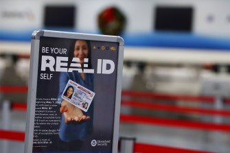 A sign in an airport that says 'Real ID' on it with a person holding a drivers license card.