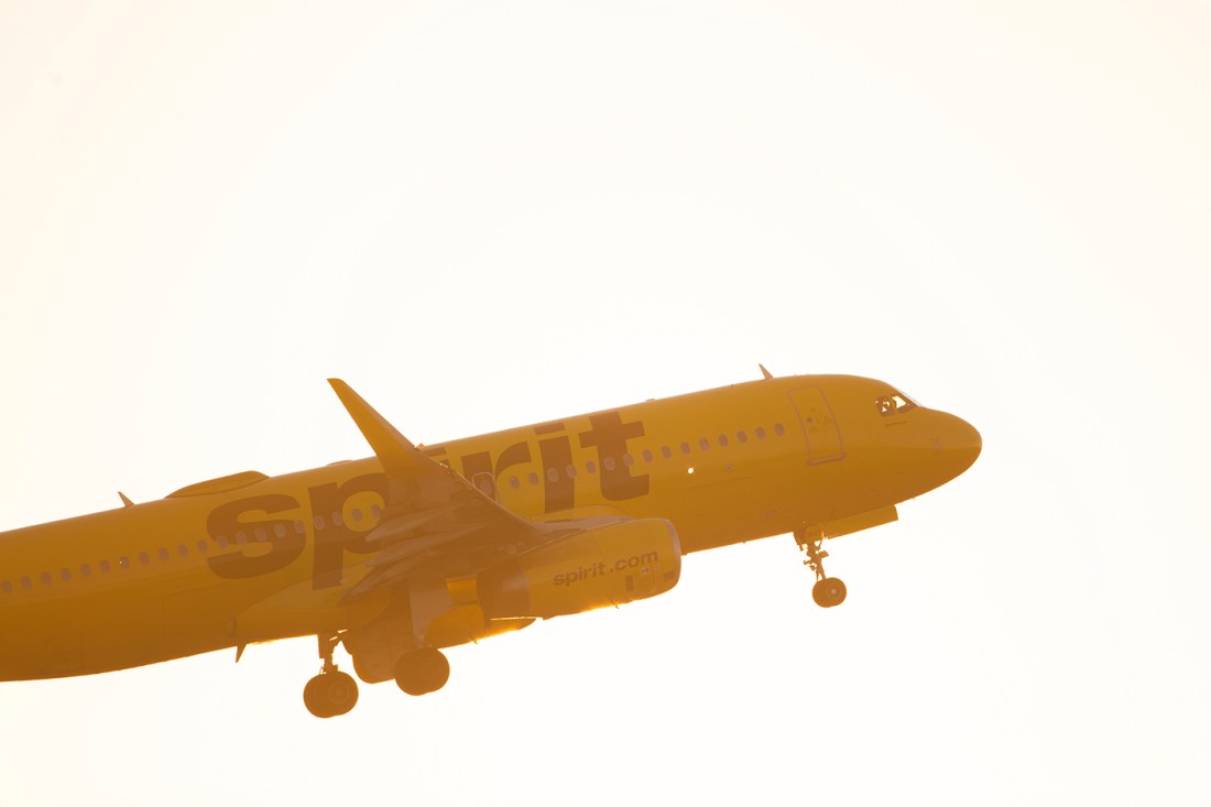 A Spirit airlines branded plane taking off at sunset.