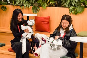 Two smiling people sit together indoors, each holding and interacting with plush toys.
