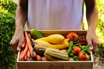 A person carrying a box full of fresh fruits and vegetables.