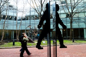 Several members of the Northeastern community walk past a stainless steel sculpture of a person walking.