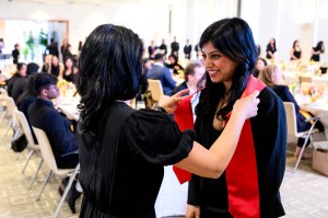A member of the Northeastern community placing a red sash around a graduate student's neck.