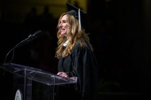 Alexandra Drane standing at a podium at the CPS Commencement wearing a cap and gown.