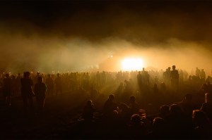 Silhouettes of crowds at people looking at a bright distant spot in the fog.