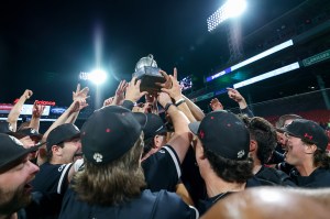 A group of people wearing matching uniforms raise a trophy together under bright stadium lights, celebrating with excitement.