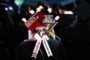 A person wearing a decorated graduation cap sits among a group of graduates during a ceremony.