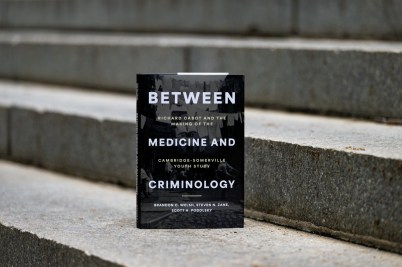 The book "Between Medicine and Criminology" stands upright on outdoor stone steps.