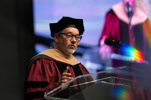 A speaker in academic regalia at a commencement podium.