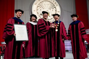 Group of people in academic regalia standing on stage during a commencement ceremony.