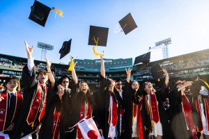 Graduates throw their caps into the air at Fenway Park during Northeastern’s 2025 Commencement ceremony.
