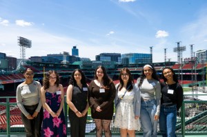 Seven smiling students pose at Fenway Park on a sunny day.