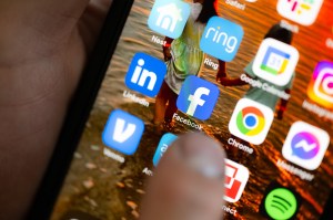 A person's thumb hovers over the Facebook icon on a smartphone.
