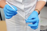 A gynecologist wearing blue gloves holding a pap smear tool.