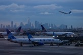 Airplanes on a runway with a city skyline in the background.