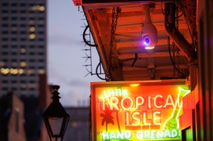 A glowing neon side that says 'TROPICAL ISLE' in orange letters mounted on a building exterior at dusk.