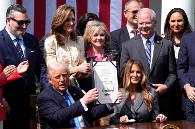 President Donald Trump holds up the signed Take It Down Act during a White House Rose Garden ceremony, joined by First Lady Melania Trump and supporting lawmakers.