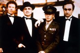 Cast members of The Godfather pose for a publicity photo in formal attire, with Al Pacino in military uniform and the others in tuxedos.