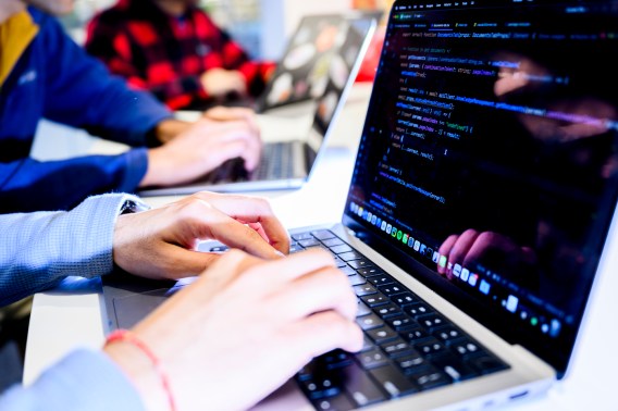 The hands of two people sitting at two different laptops typing next to each other.