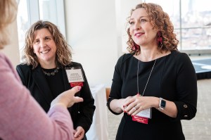 Jennifer Kirwin and Margarita DiVall stand side by side and speak to someone who stands right next to the camera lens. They are both wearing black shirts and name tags.