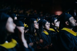 Graduates wearing black gowns with gold accents sitting in a darkened Meridian Hall for the Toronto graduation.