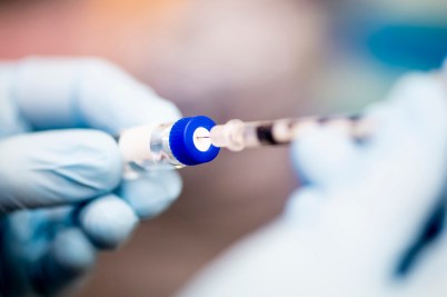 A person filling a syringe with gloved hands.