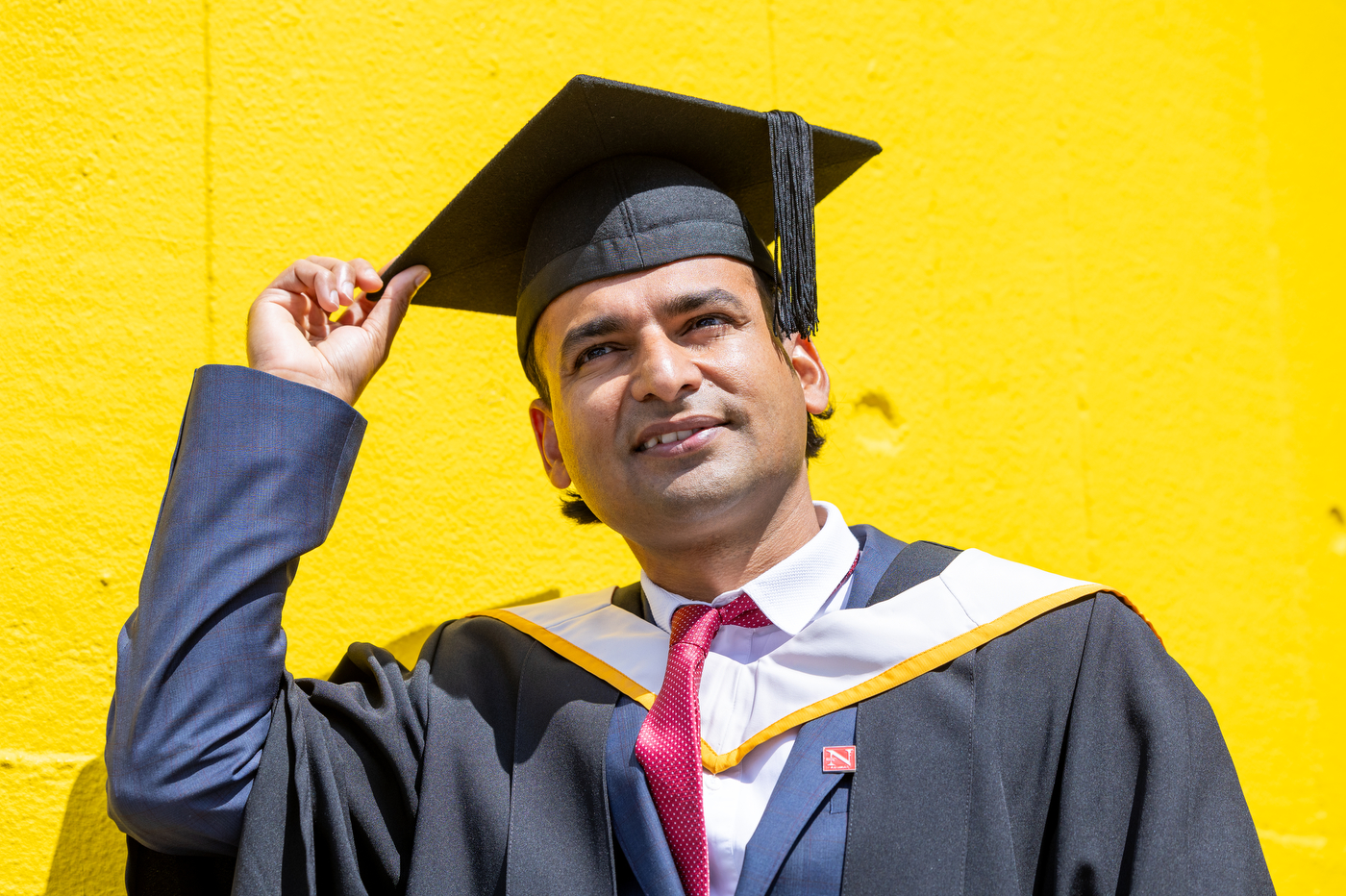 A student wearing a cap and gown poses in front of a yellow background.