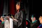 A graduate speaks at a podium during a commencement ceremony.