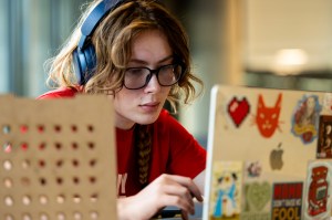 A person focuses on a laptop while wearing headphones indoors.