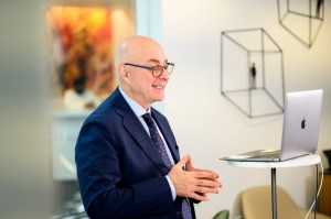 Northeastern President Joseph E. Aoun speaks during a virtual conference, smiling while standing in front of a laptop.