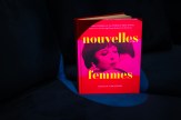 The brightly-colored book &quot;Nouvelles Femmes&quot; standing upright on a dark chair on a black background.