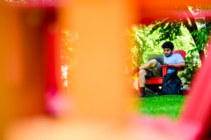 A person sits outside on a red chair, focused on a laptop, framed by bright, colorful shapes in the foreground.