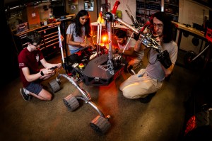 Members of the Mars rover team sitting and kneeling around the rover, working on various components.