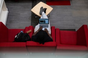 A person sits on a red couch using a laptop, viewed from above.