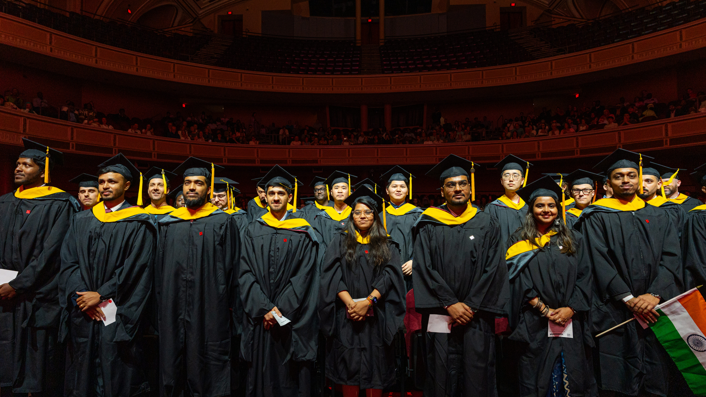 Graduates in academic regalia stand and smile a ceremony.