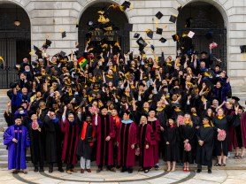 Graduates in caps and gowns celebrate on the steps outside a historic building.