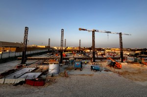 A construction site at sunset with cranes, scaffolding, and heavy equipment set up for a large-scale building project in Qatar.
