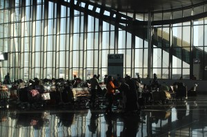 Travelers wait with luggage carts in a sunlit terminal at Hamad International Airport in Doha, Qatar.