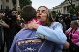 A woman embraces someone outside a courthouse as people and media gather around.