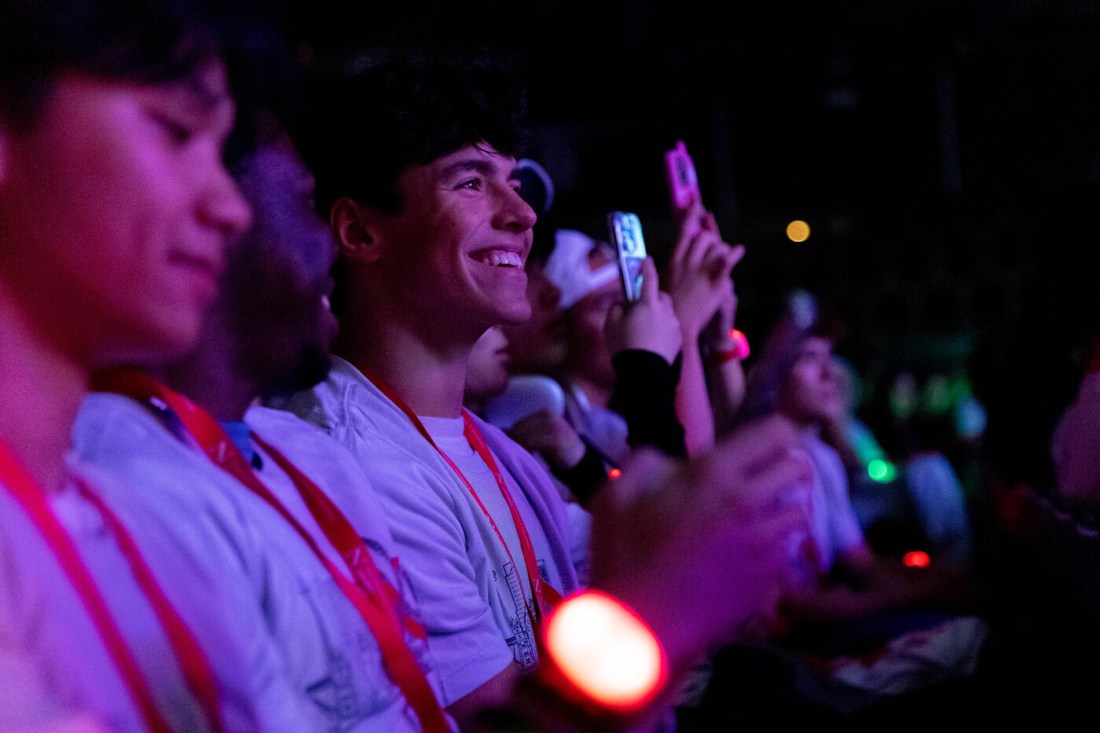 Students wearing red lanyards smile and take photos during a brightly lit orientation event.