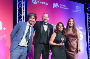 Four people wearing business professional clothing posing in front of a pink and purple styled backdrop at an awards ceremony.