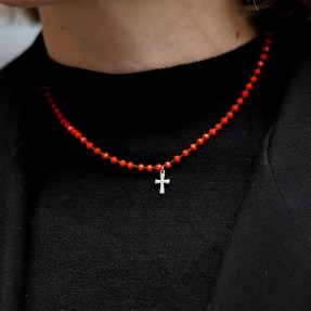 A close up shot of a person wearing a black sweater with a red beaded necklace that has a small cross pendant.