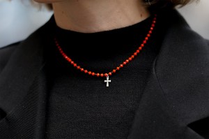 A close up shot of a person wearing a black sweater with a red beaded necklace that has a small cross pendant.