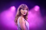 Taylor Swift performs on stage under purple lights, glancing over her shoulder during a concert.