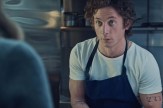 Screen capture of a character from the TV show &#039;The Bear&#039; wearing a white t-shirt with a black apron over top.